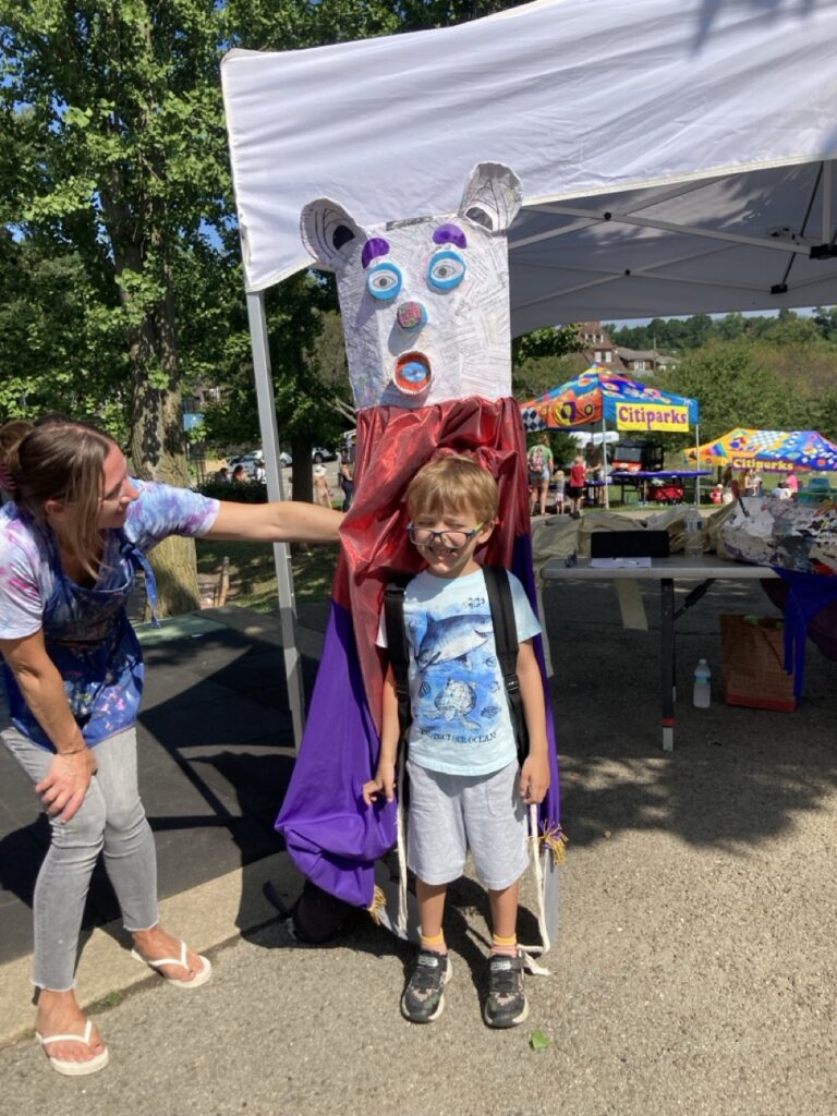 A little boy stands under a paper mache bear head.