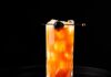 Standing Drama: Chocolate-Cherry Gin Cocktail A tall glass with a chocolate-cherry gin cocktail that's orange and has a cordial cherry on a pick as a garnish.