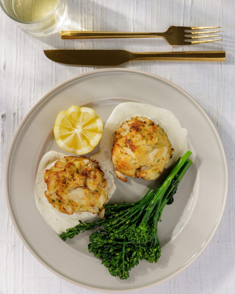 A plate of seafood with two crab cakes, a lemon half, and greens.