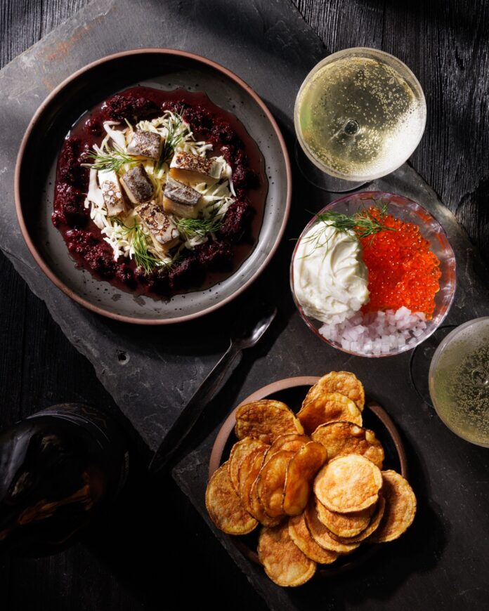 A black table with dishes of caviar, chips, chopped fish over rice, and vegetables.