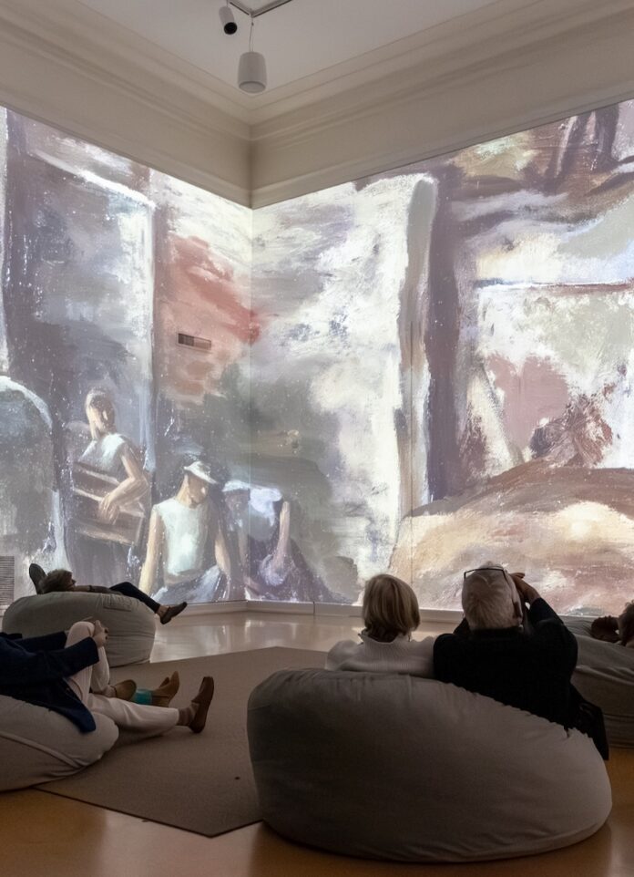 People on bean bags look up at an art exhibit projected onto the museum walls.