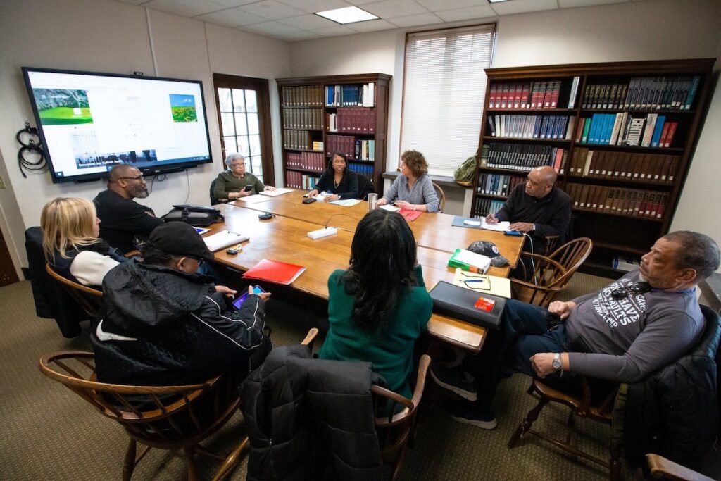 A group of Their Story filmmakers sit around a table, looking at a screen on the wall.