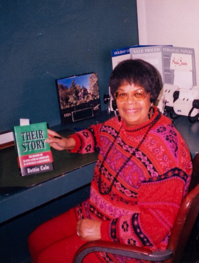 Bettie Cole sits in a red sweater with her book "Their Story."