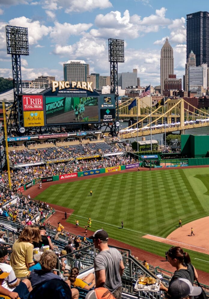 A baseball game with a large crowd inside PNC Park in Pittsburgh with the skyline behind the stadium.