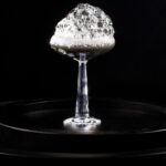 A cocktail that's black in color with a bubbly foam over top.