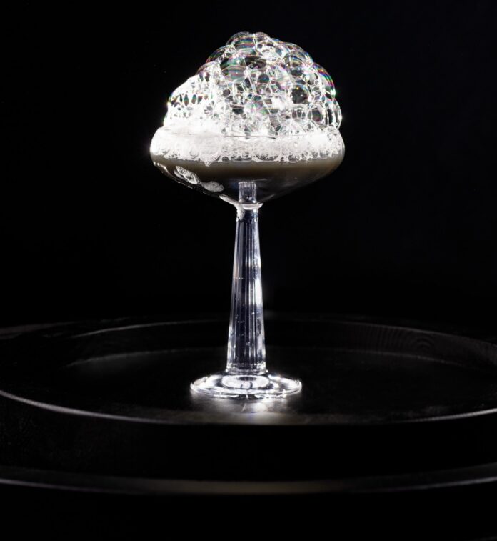 A cocktail that's black in color with a bubbly foam over top.