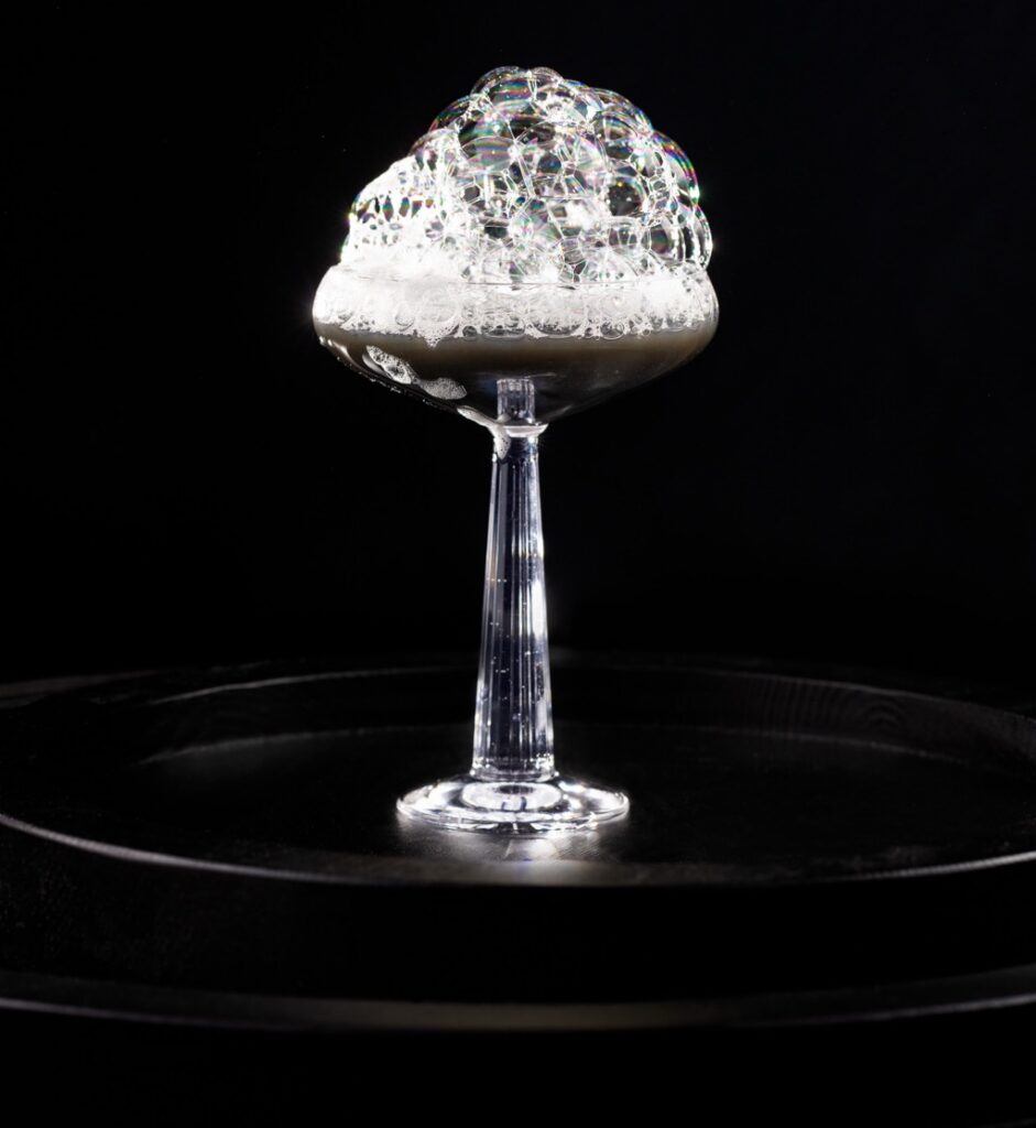 A cocktail that's black in color with a bubbly foam over top.