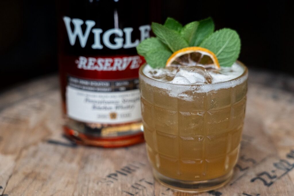 A whiskey cocktail sits beside a bottle of wigle whiskey.