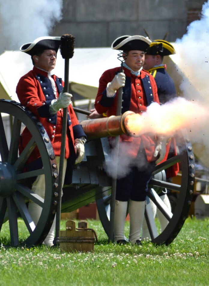 Three re-enactors working a canon as it fires.