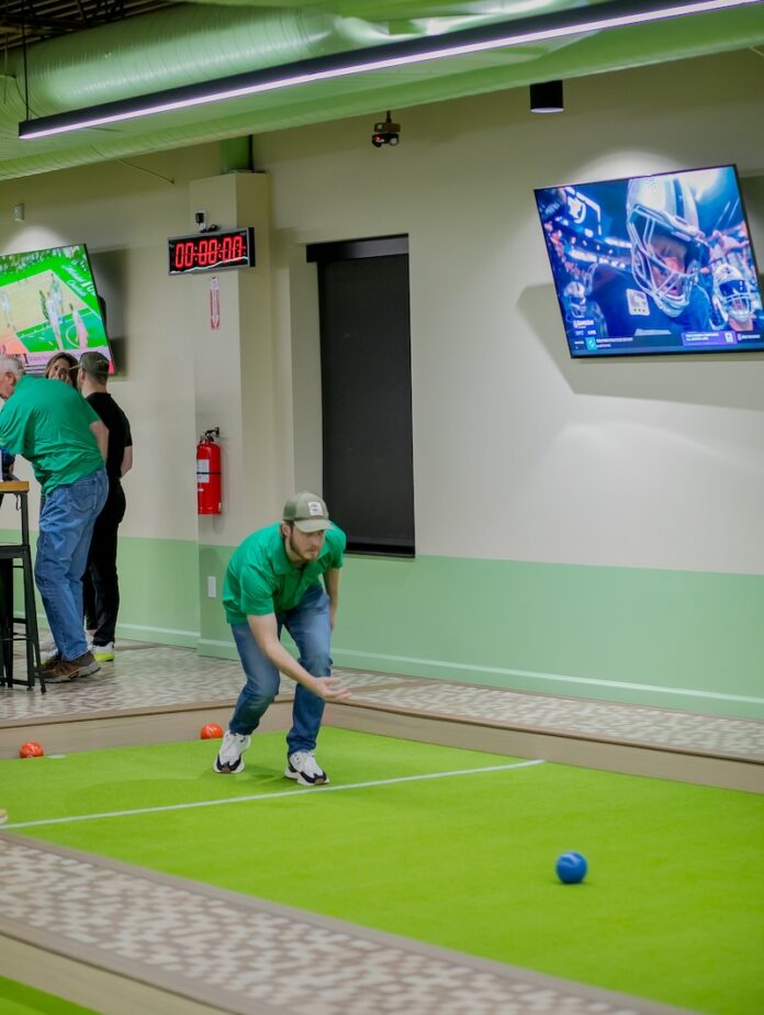A person throws a ball down a green bocce court.