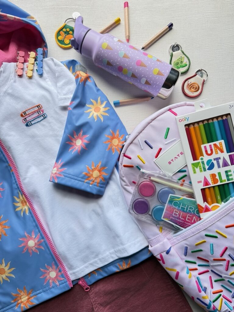 A blue jacket with flowers on it next to a purple water bottle and purple backpack with sprinkles.