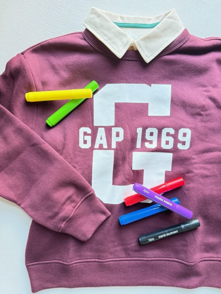 A kids Gap sweatshirt with a white collar and markers on the sweatshirt.