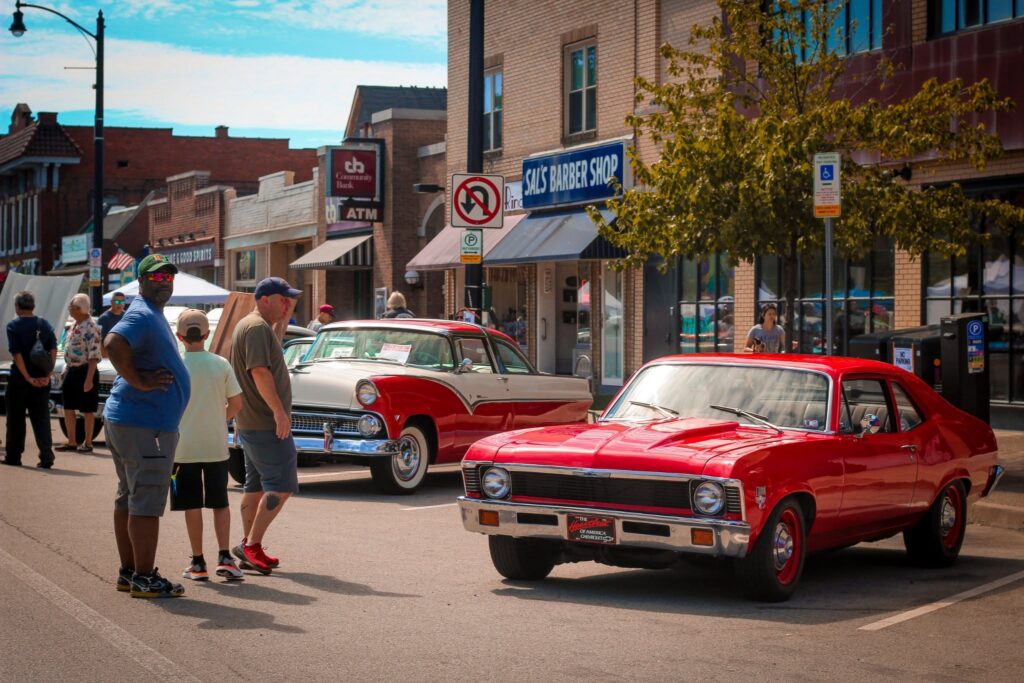 People walk past classic cars on the streets of Brookline.