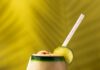 Disney Adult Dole Whip Cocktail A short cocktail glass with a frozen Dole-Whip cocktail with a lime garnish and straw on a green background.