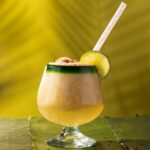 A short cocktail glass with a frozen Dole-Whip cocktail with a lime garnish and straw on a green background.