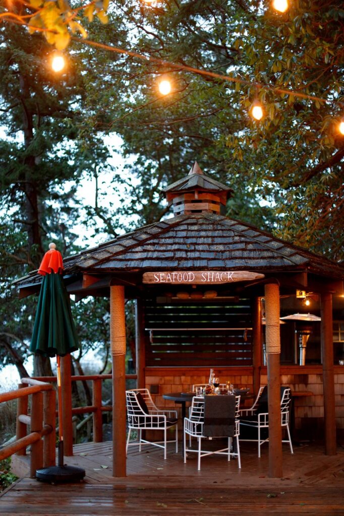An outdoor bar hut with bar seats around it and lights in the trees overtop.