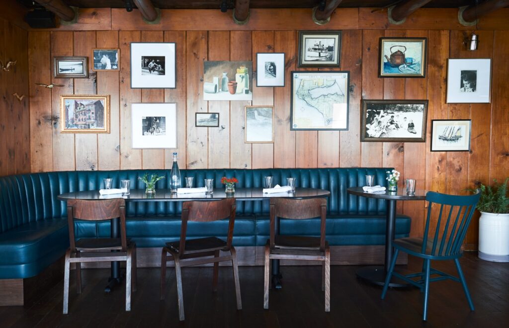 A blue booth along a wall under photographs with chairs on the other side of the table.