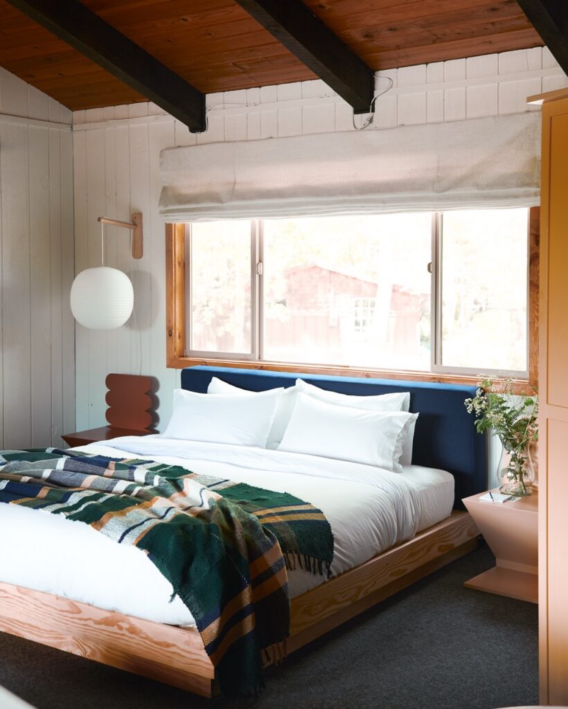 A bed room with a window above the bed, white pillows, and wood ceilings.