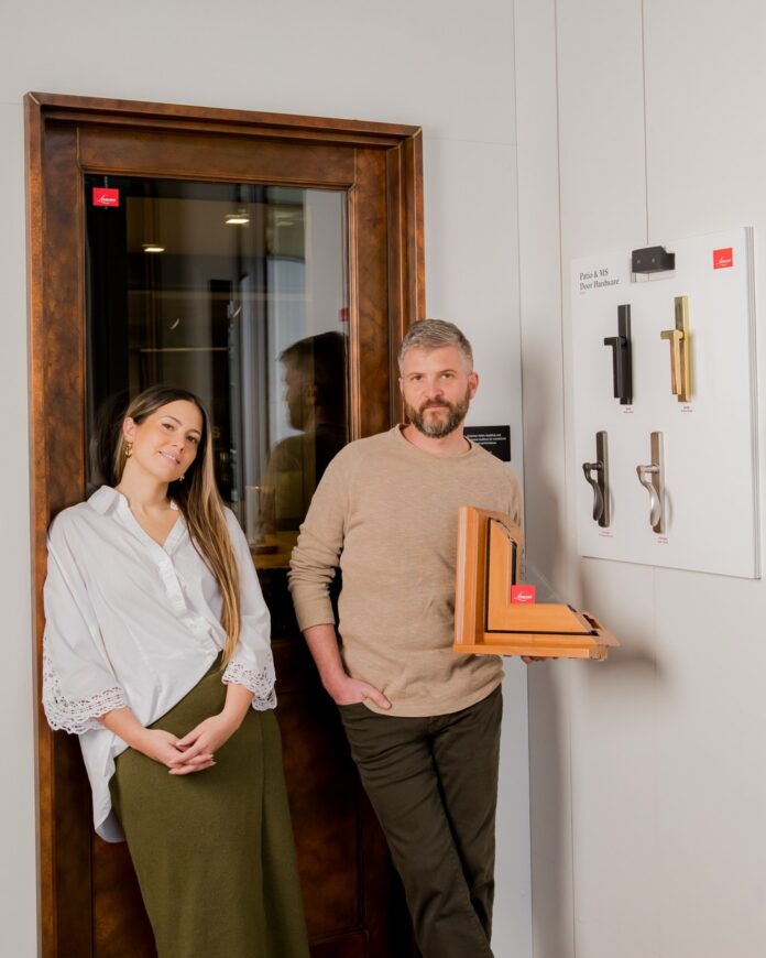 Jeremy Davis and Brandi Cowen stand in front of a door as Jeremy holds a corner sample of wood work.