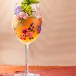 A tall wine glass with florals on the glass holds a Frozen Melon Gin Spritz with mint as a garnish.