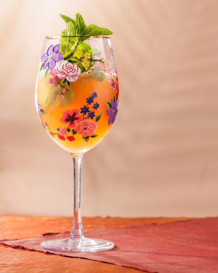 A tall wine glass with florals on the glass holds a Frozen Melon Gin Spritz with mint as a garnish.