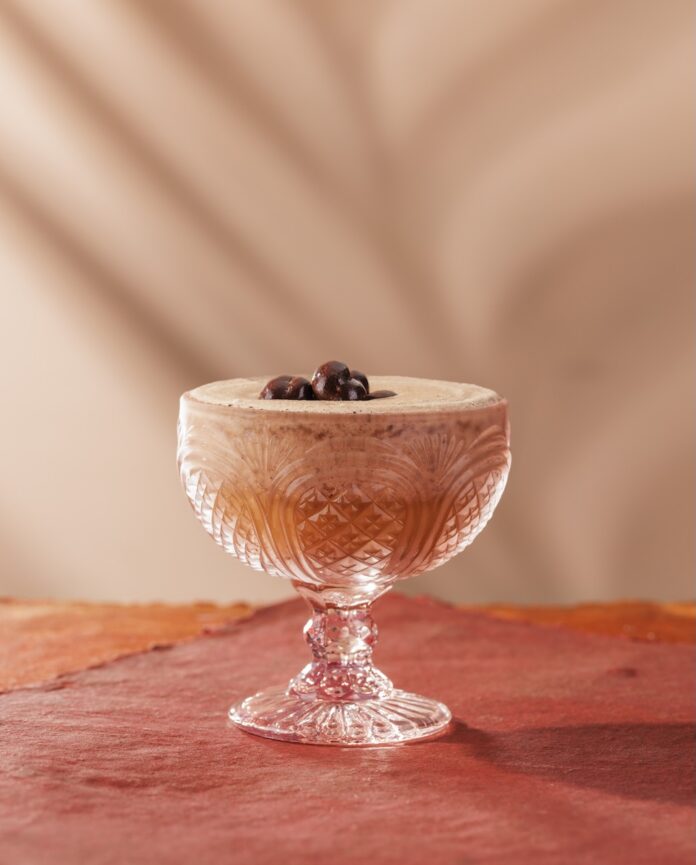 A short cocktail glass with a frozen Espresso Martini with three coffee beans on top on a pink background.