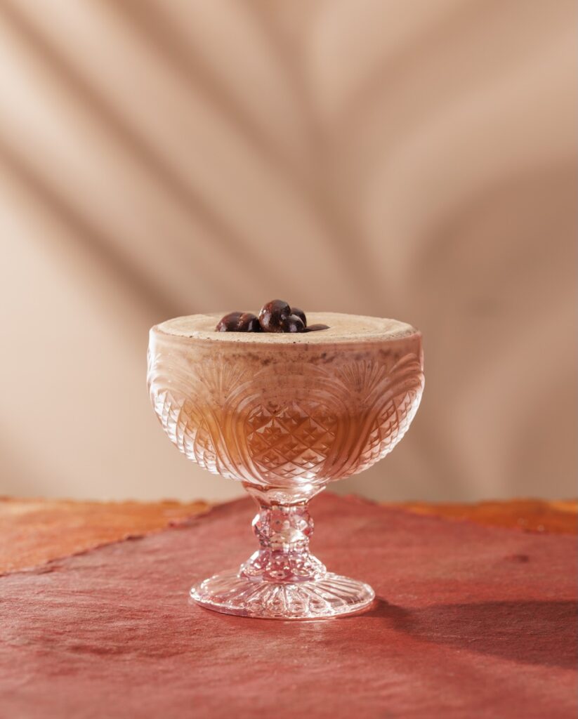 A short cocktail glass with a frozen Espresso Martini with three coffee beans on top on a pink background.