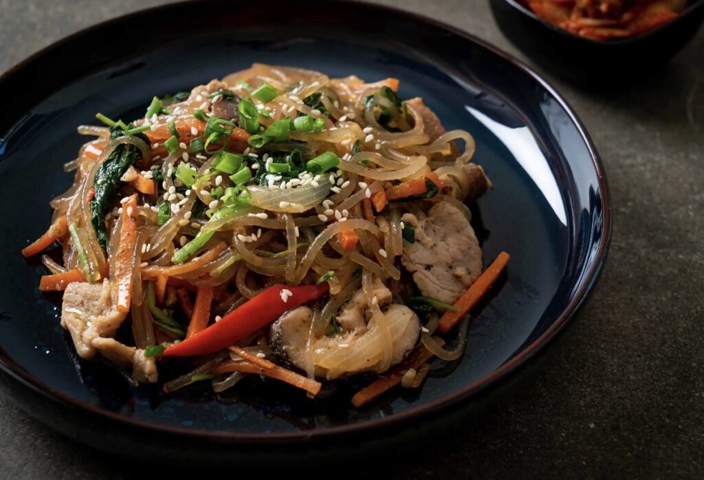 A plate of Chinese stir fry with chicken and vegetables on a table.