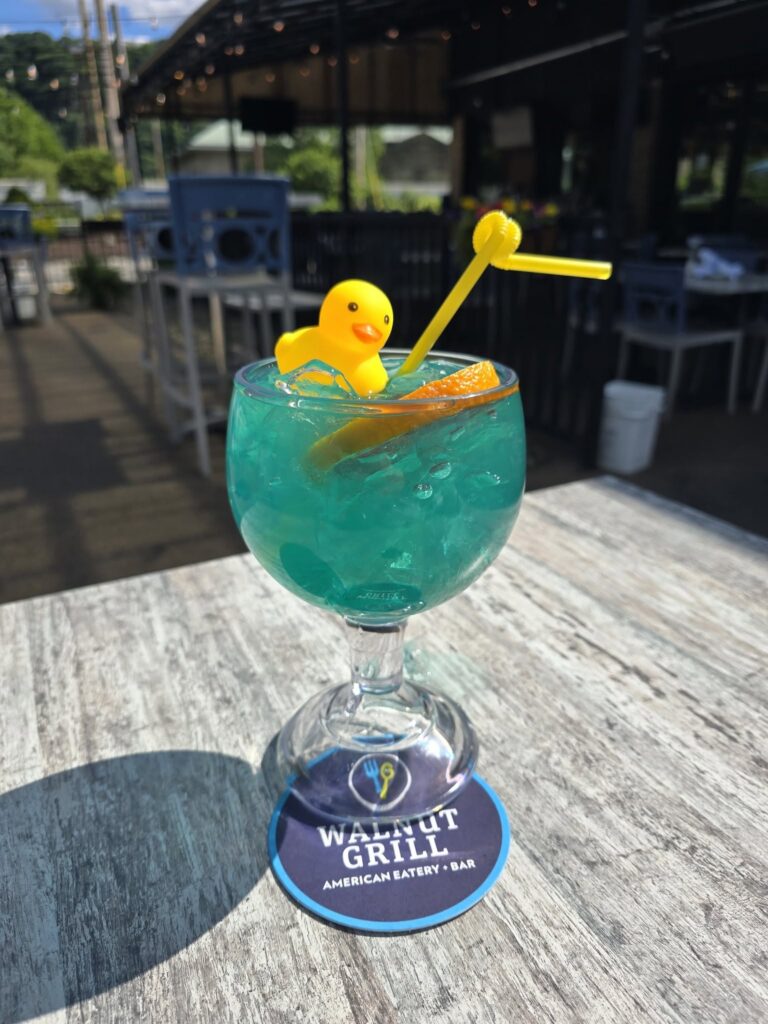A blue cocktail on a patio table with a rubber duck and curly straw in it.