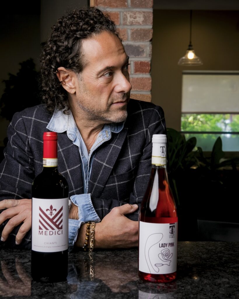 Jason Grant sitting behind two bottles of Medici Importers Global wine as he looks off to the right.