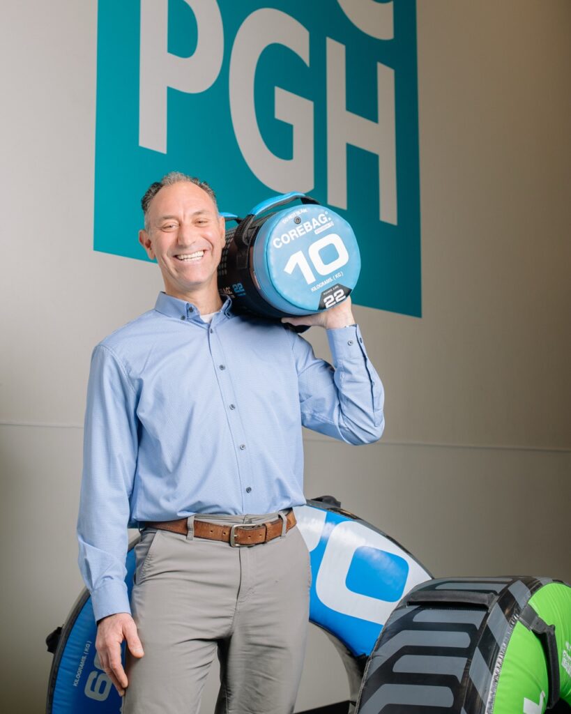 Jason Kunzman holds a 10 pounds weight bag in front of two weight tires.