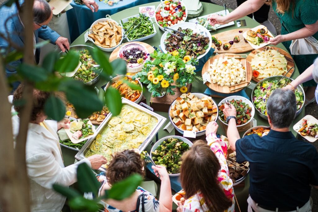 People gather around a table full of self-serve food from cheeses to bread to veggies and salad.