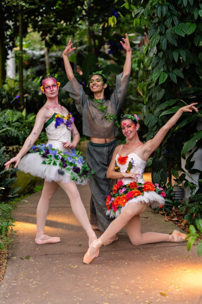 Three dancers pose in floral and greenery outfits.