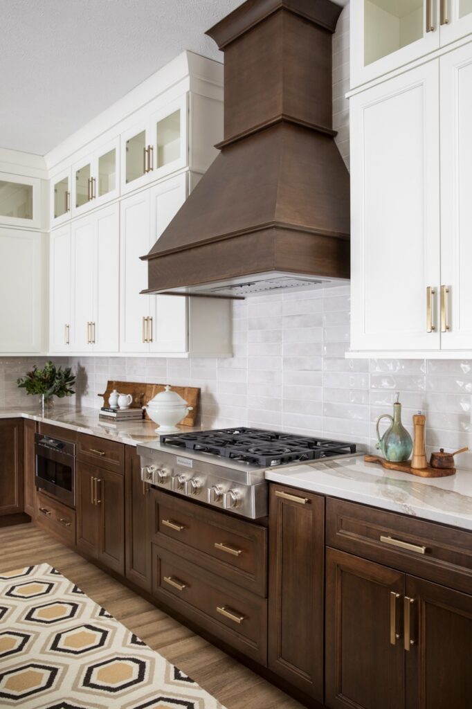 A stove with a white backsplash and brown oven hood overhead.