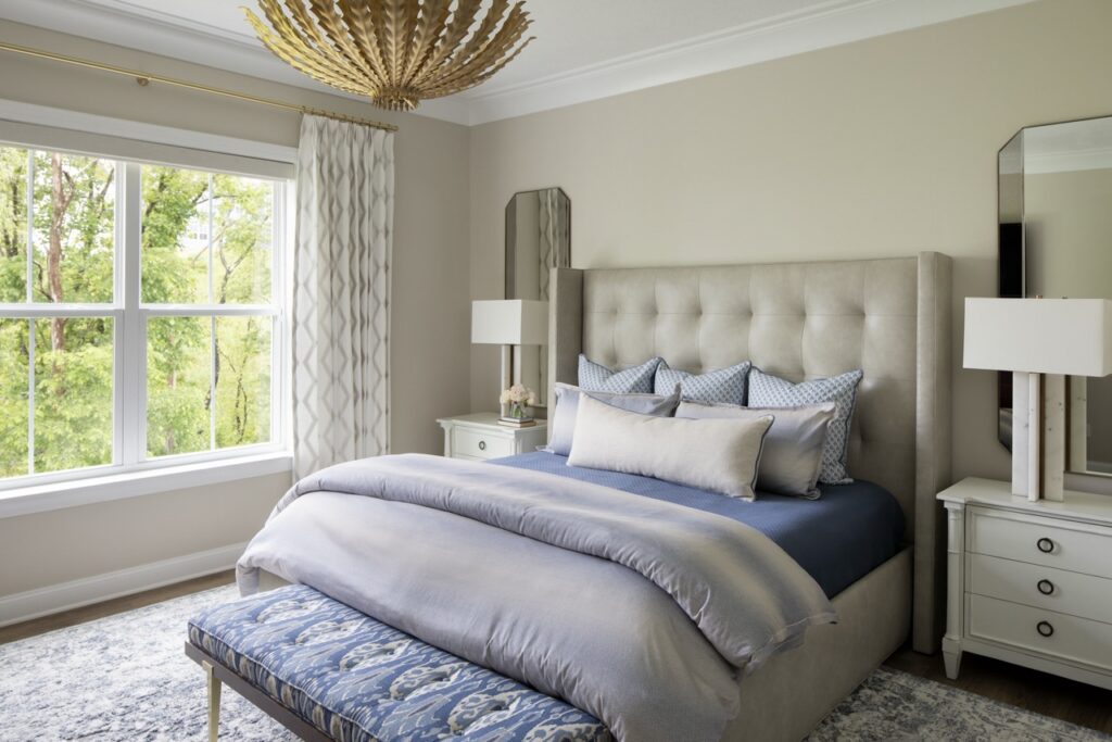 A bedroom with a large blue and white bed, big window and white night stands on both sides of the bed.