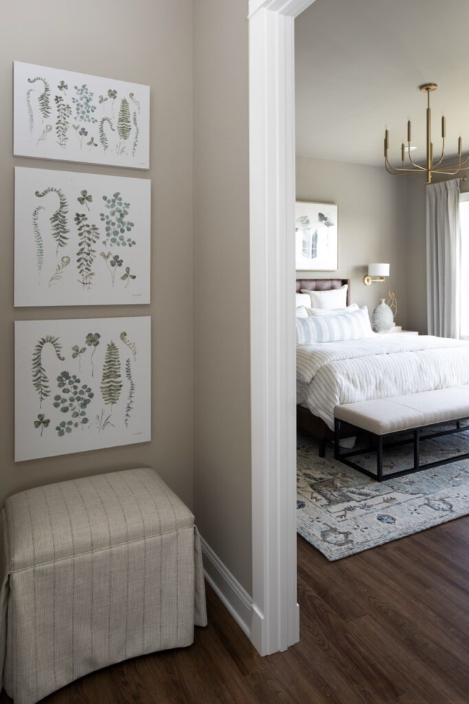 Three prints hang on a wall over top of each other while the wall peaks into a white bedroom.