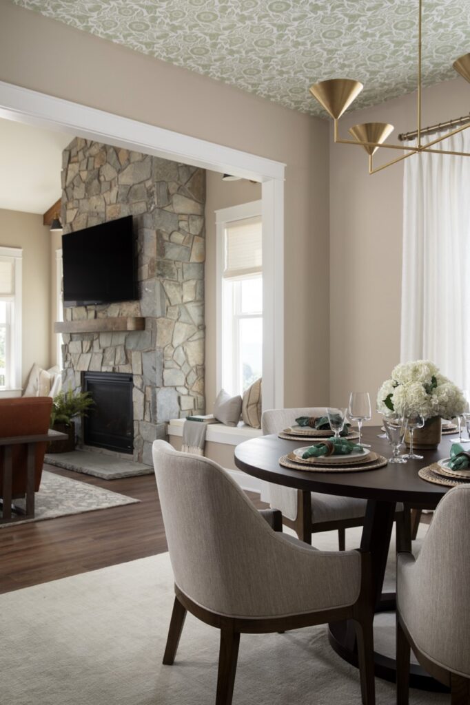Two chairs sit at a round dining table with a doorway leading to the living room stone fireplace and TV.