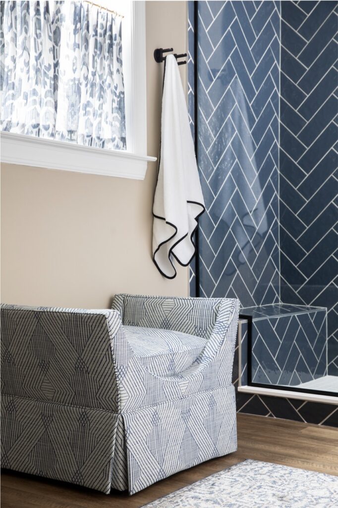 A grey chair beside a glass shower and a towel hanging off the wall.