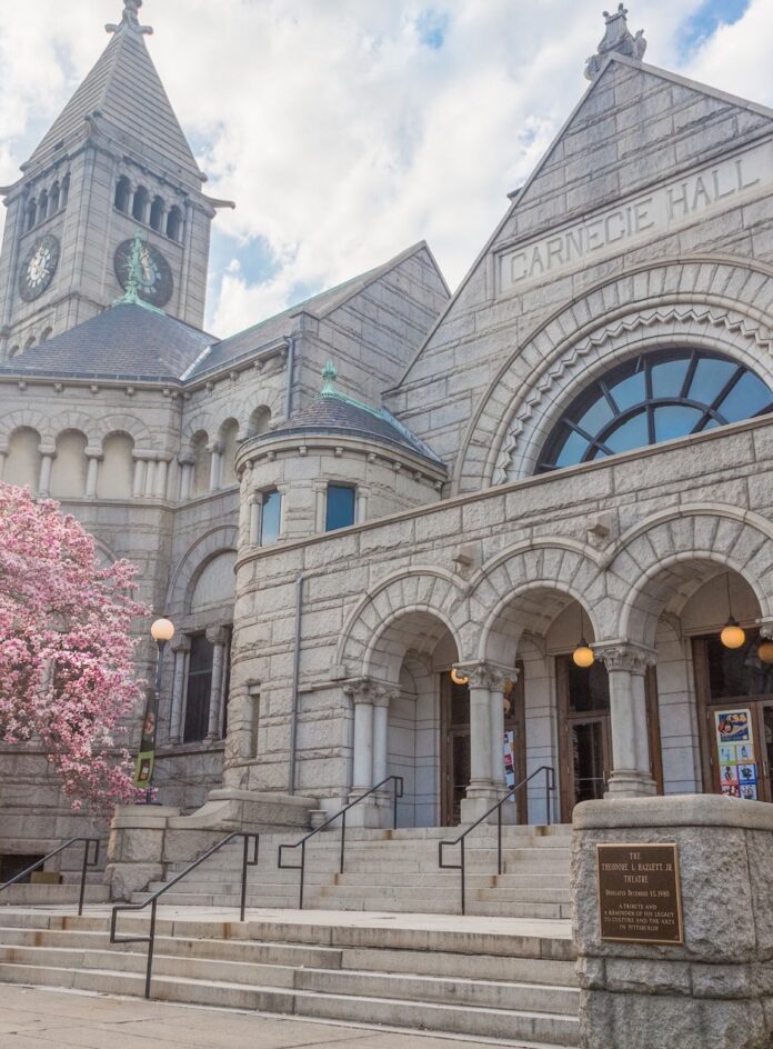 The outside of where the New Hazlett Theater is in Carnegie Music Hall with a pink tree blossoming beside it.