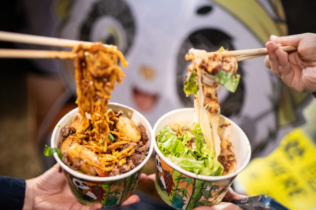 Two people lift noodles from two bowls.