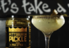 Where to Get Pickle Foods and Drinks in Pittsburgh If You’re Skipping Picklesburgh A pickle martini with a black salt rim on the glass beside a pickle jar from Pittsburgh Pickle Co.