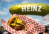Your Guide to Picklesburgh 2026: What to Eat, See, and Dill Before You Leave A chicken sandwich with pickles on it in front of the inflatable Heinz pickle balloon.