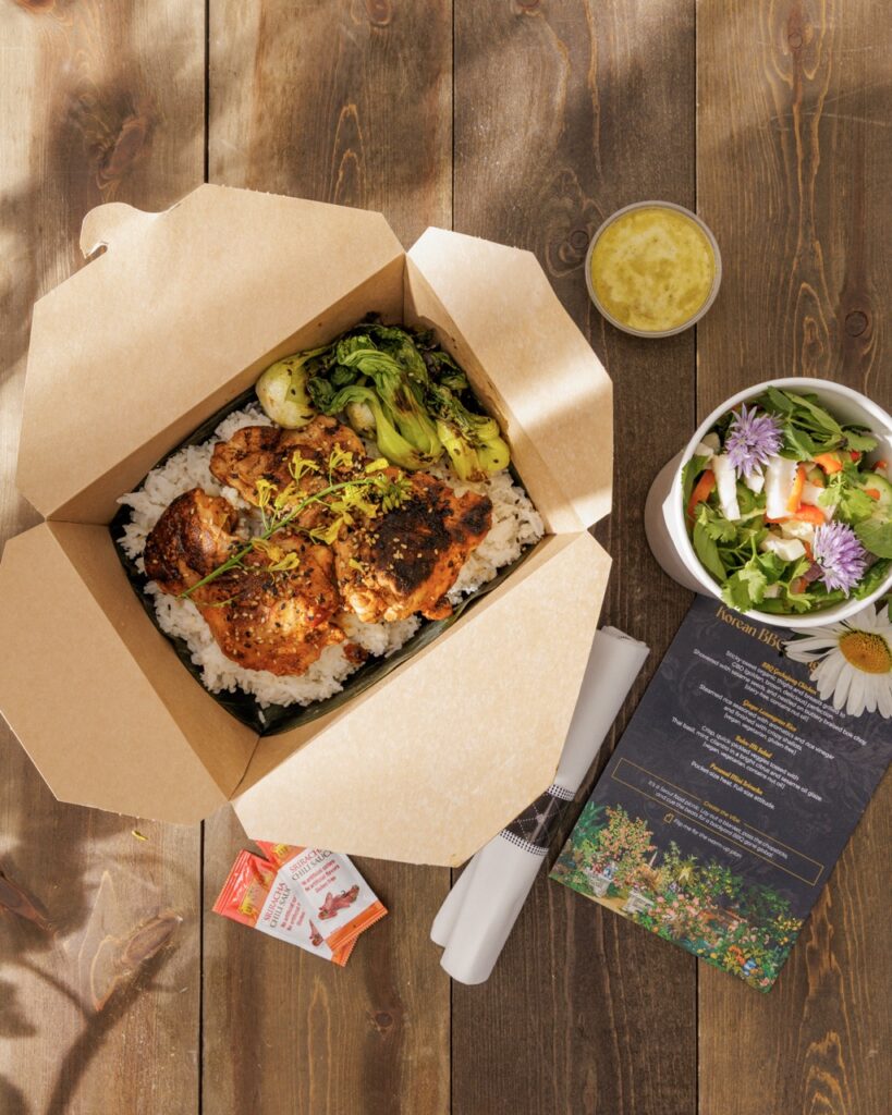 A brown box of Korean chicken on rice with a side salad.