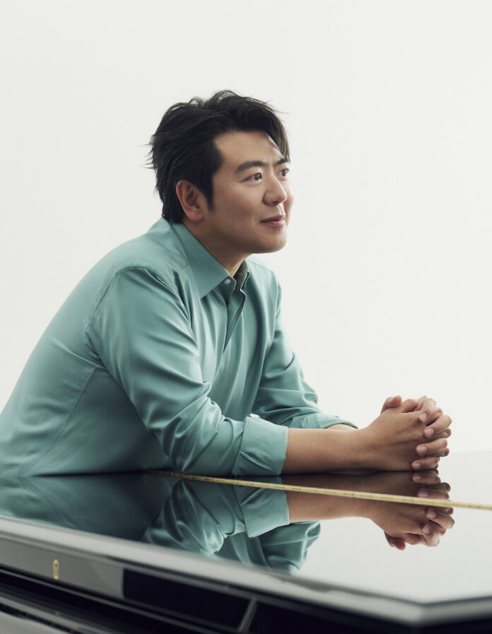 Lang Lang in a blue button up shirt leaning over a black piano.