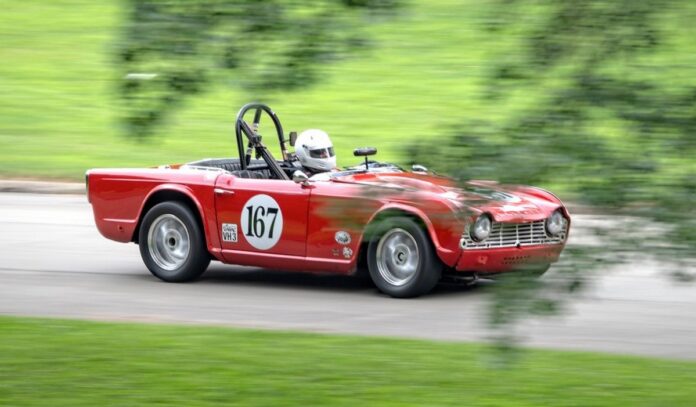 A vintage car with red paint and a white number spot with a racer in the seat.