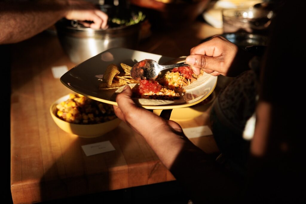 A person spoons food onto their plate from a potluck.