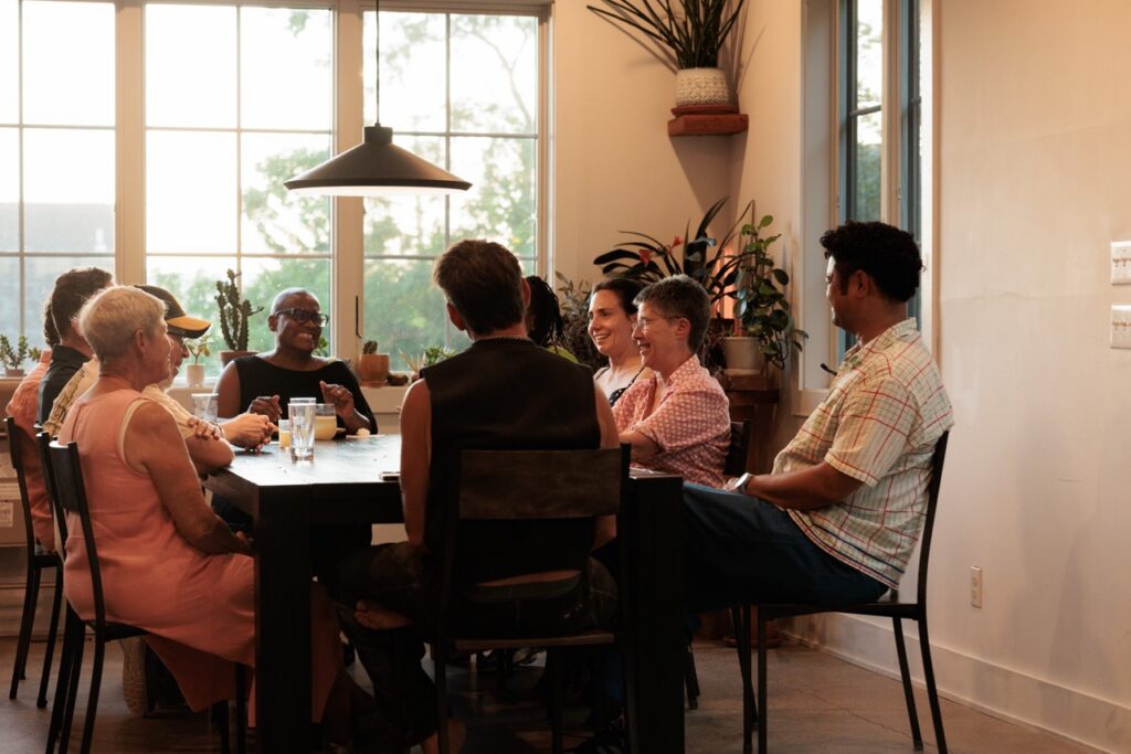People sit and laugh at a dining table inside with a light overhead.