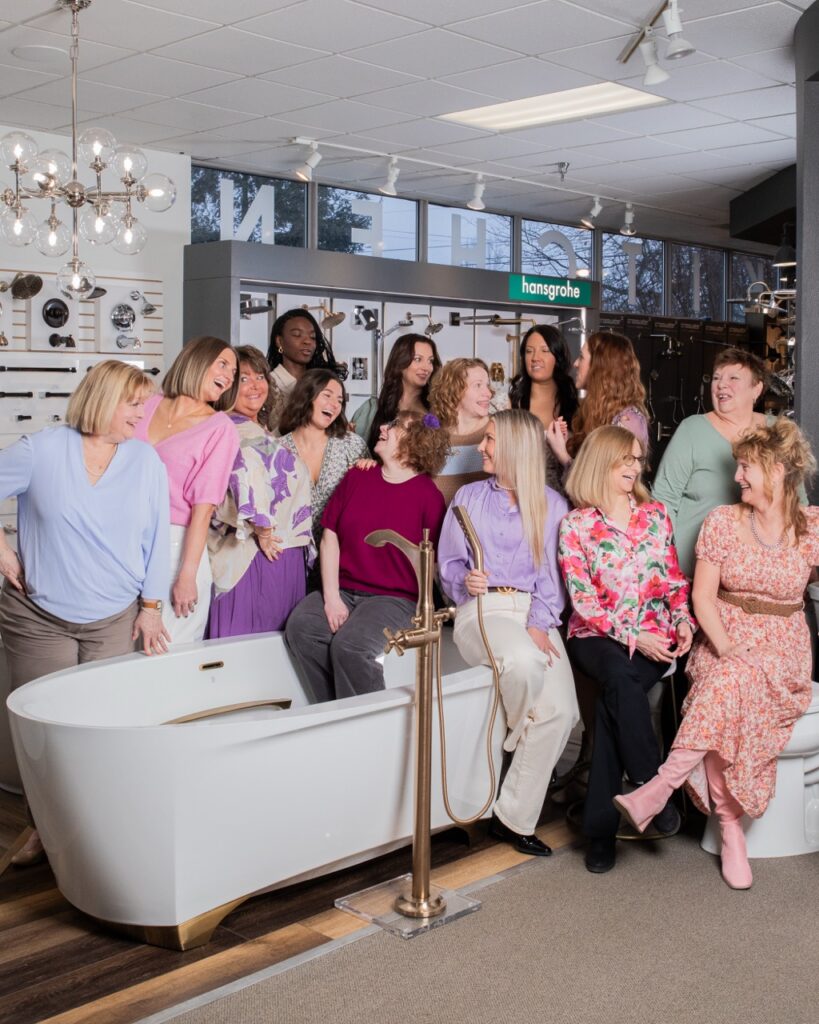 A group of ladies from SPLASH sit on and around a white bath tub with a gold faucet.