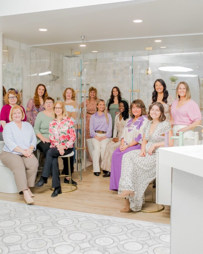 The ladies of SPLASH inside a bathroom fixture with a glass shower and tile.