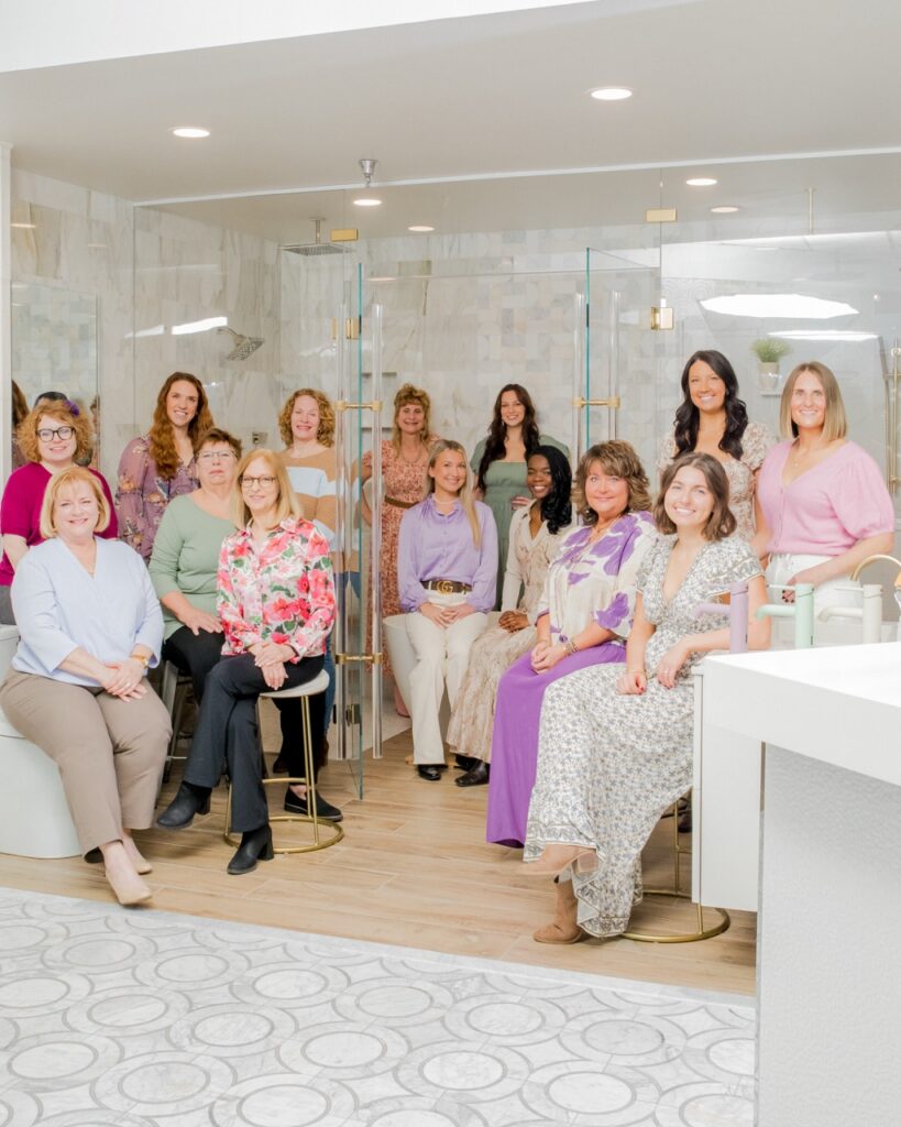 The ladies of SPLASH inside a bathroom fixture with a glass shower and tile.